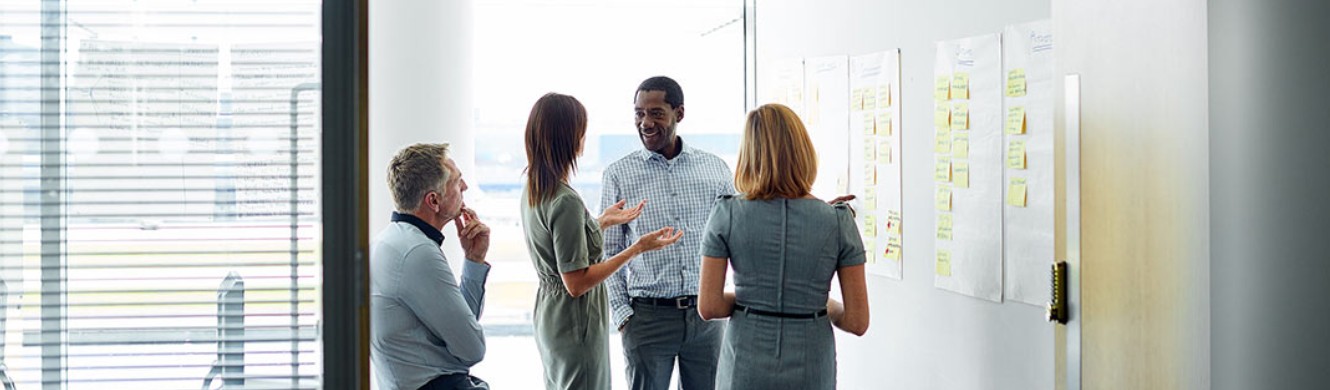 Two men and two women stand discussing a chart on the wall 